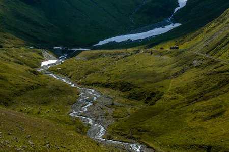 A verdant valley with a winding river starting from a glacier further upstream and cows grazing on the valley floor.の写真素材