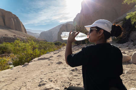 Woman drinking water from bottle under sunの写真素材