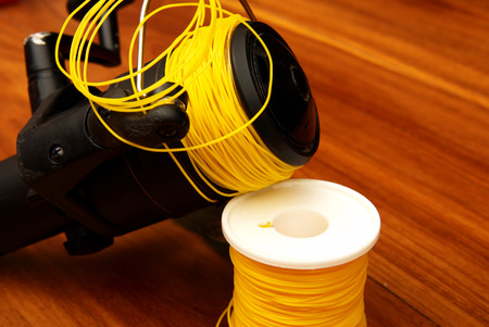 Fishing reel with yellow fishing line rolled onto the reel. The rest of the fishing line is on the role in the backgroundの写真素材