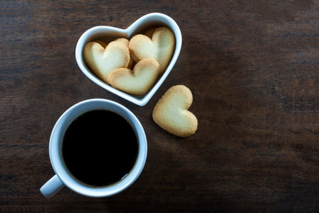Coffee mug with heart-shaped biscuits in a white heart-shaped cup on a rustic wooden floor, flat lay, space for text, Valentine's day concept.の写真素材