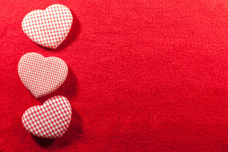 Three hearts made of cloth with red white checkered pattern arranged on a red velvet background with copy space, flat lay, Valentine's day concept.の写真素材