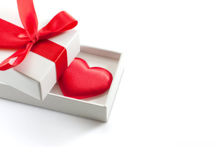 Red heart shape inside a white gift box tied with red ribbon on white background with copy space,...