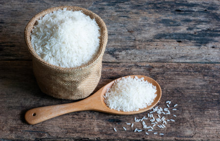 Jasmine rice in sack and in wooden spoon on a rustic wooden table.の写真素材