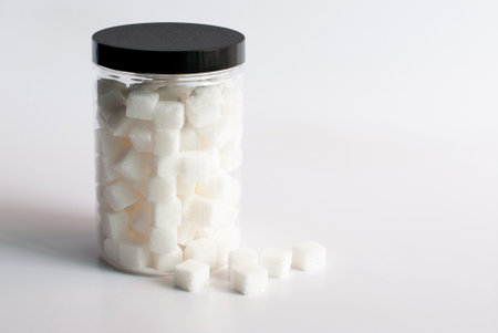 Sugar cubes in a transparent jar on a white background.