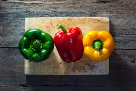 Colorful of bell peppers, green, red, yellow with a wooden cutting board on rustic wooden...