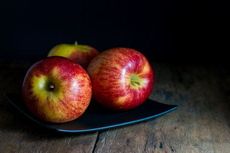 Delicious red apples are placed on a black square ceramic plate on a rustic wooden floor.の写真素材
