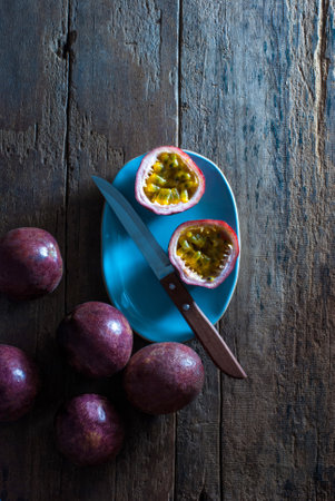 Slice and whole passion fruits with a kitchen knife in a pastel blue ceramic tray on a rustic wooden floor, top view.の写真素材