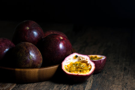 Slice and whole passion fruits in a wooden tray on a rustic wooden table.の写真素材