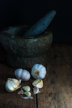 Several heads of garlic with mortar and pestle put on a rustic wooden floor.の写真素材