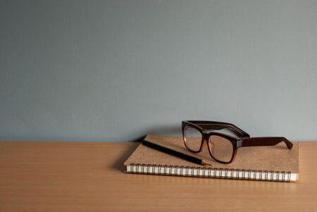 Glasses, pencils, and notebooks on a wooden table. Space for text.