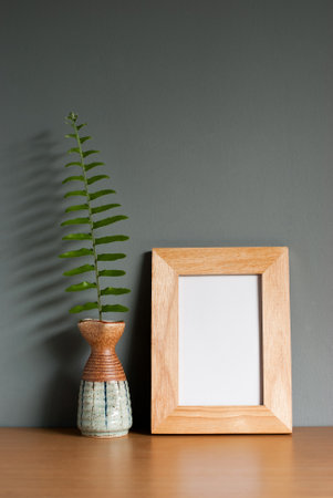 Light wooden frame mockup with fern leaves in a ceramic vase on wooden table and grey background. blank space, vertical image, still life, copy space.の写真素材