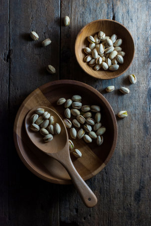 The pistachios are in a wooden tray with a wooden ladle. And in a wooden cup placed on a wooden table, top view.の写真素材