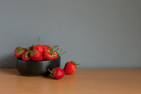 Strawberries are placed in a black ceramic cup on a wooden table and grey background. Space for text.の写真素材