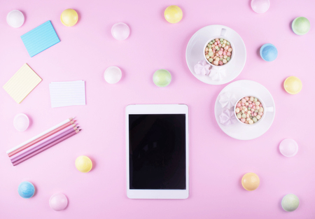 Workspace. Pink pastel flat lay with tablet, two cups, pencils and sweeties.の写真素材