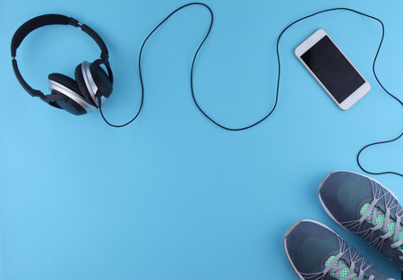 Flat lay shot of sneakers, earphones and phone on blue background with copy space for your text....