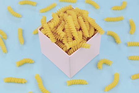 Uncooked italian pasta girandole on blue trendy background. Colorful diet and healthy food concept.