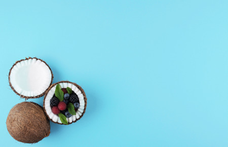 Fruits of coconuts on blue background with mix of berries. Colorful diet and healthy eating concept. Flat lay style.の写真素材