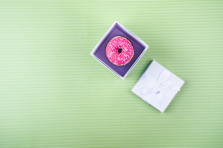 Donut covered with icing, top view on trendy green background. Flat lay style.
