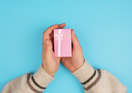 Top view of hands holding a small box with a gift and a ribbon on a blue background.の写真素材