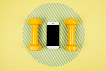 Orange dumbbells with smartphone on yellow and green background. Sports fitness cardio martial artの写真素材