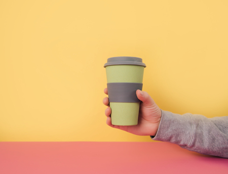 Hand holding take away coffee cup on colorful paper background. Recycling consept.