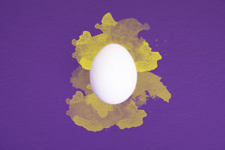One white egg on ultra violet background with yellow watercolor splatters.の写真素材