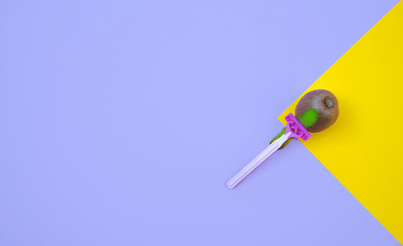 Kiwi fruit and razor on violet and yellow background. Hair removal concept.の写真素材