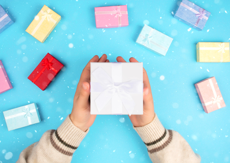 Top view of hands holding a small box with a gift and a ribbon on a blue background.の写真素材