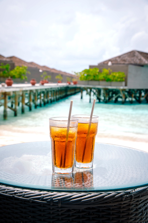 Iced tea against tropical Overwater Bungalow Resort on the beachの写真素材