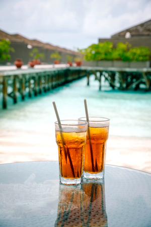 Iced tea against tropical Overwater Bungalow Resort on the beachの写真素材