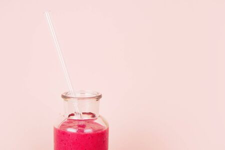 Minimalist composition of glass with raspberry smoothie and with reusable glass straw on pink backgroundの写真素材