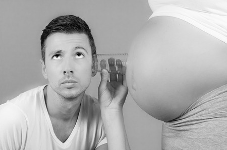 funny father listening with a glass on the belly of his pregnant wife in black and whiteの写真素材