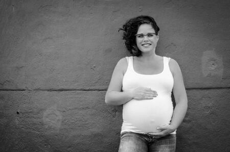 curly beautiful pregnant woman in front of a wall in black and whiteの写真素材