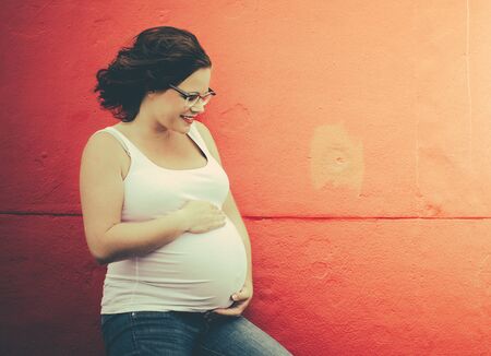 urban maternity photo of a woman looking at her belly and smilingの写真素材