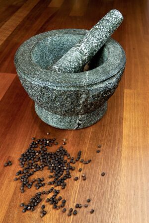 Stone mortar on a hard wood surface with peppercorns