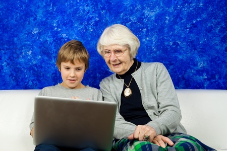 Grandmother and grandchild sitting in a sofa looking at a laptop