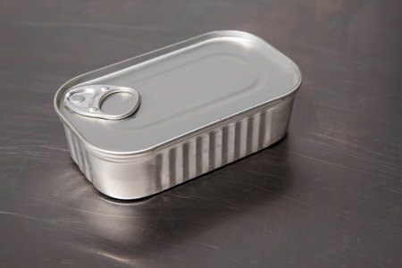 Closed tin can with preserved fish lying on a shiny tableの写真素材