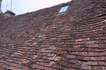 View over an old french worn out clay shingle roof, with a an iron roof window and chimneysの写真素材