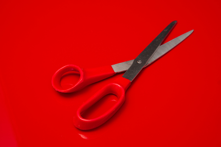 A cheap tailor's scissors with red plastic handles lying on a red backgroundの写真素材