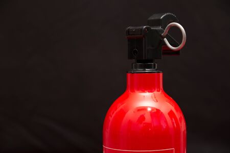 the top nozzle of a small fire extinguisher with a securing pin attached in front of a black backgroundの写真素材