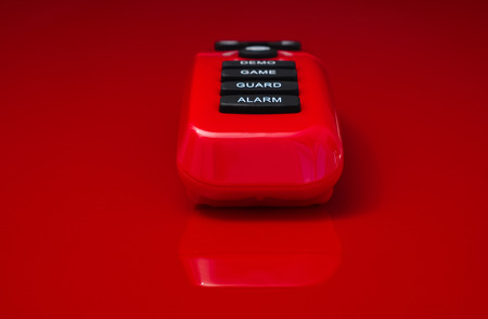 red plastic remote control with black rubber buttons with the text alarm, guard, game and demoの写真素材