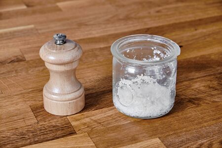 Pepper mill of light wood and a salt jar of transparent glass, standing on a table of dark brown laminated hardwoodの写真素材