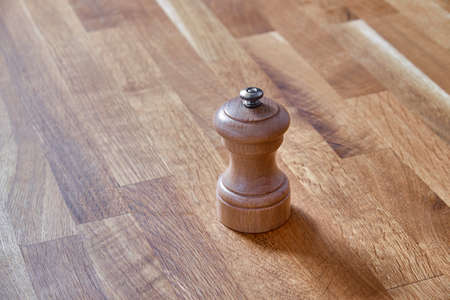 Pepper mill of light wood, standing on a table of dark brown laminated hardwoodの写真素材
