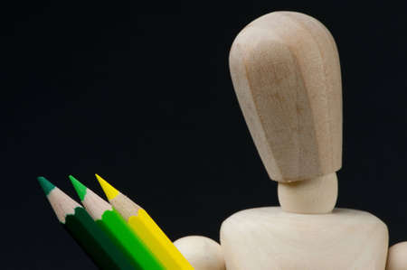 An artists mannequin holds 3 coloured pencils and is looking down at them. Isolated on blackの写真素材