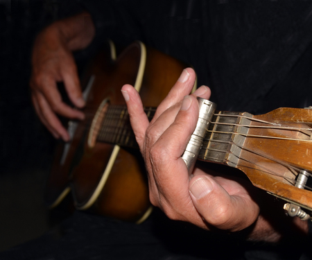 Closeup view of hand and steel slide playing an old acoustic guitar at night.の写真素材