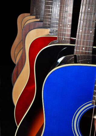 A selection of blue, red, black and natural wood colored acoustic six string guitars isolated on a black background.の写真素材