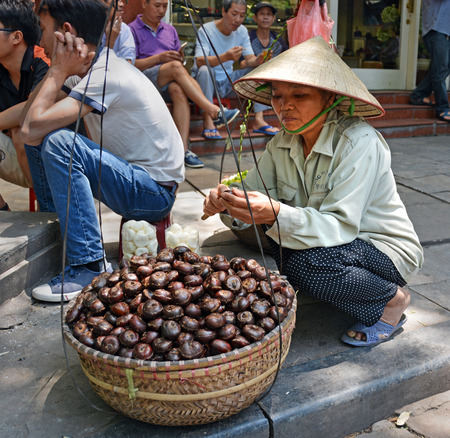 Hanoi Vietnam  April 14 2015: Woman street vendor peeling roasted Chestnuts from a basket on the pavement.のeditorial素材