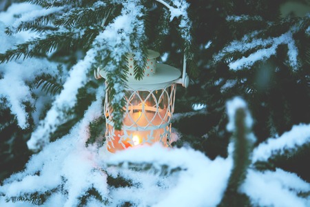 Christmas lantern with burning candle on winter nature background.の写真素材