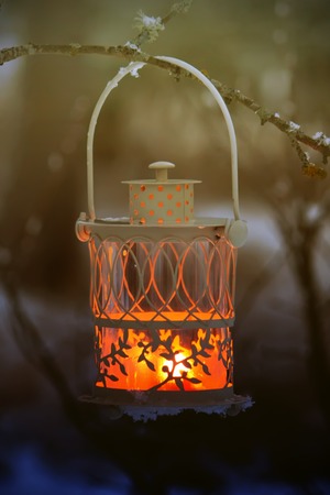 Christmas lantern with burning candle on winter nature background.