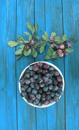Ripe plums in a cup on a wooden blue aged backgroundの写真素材